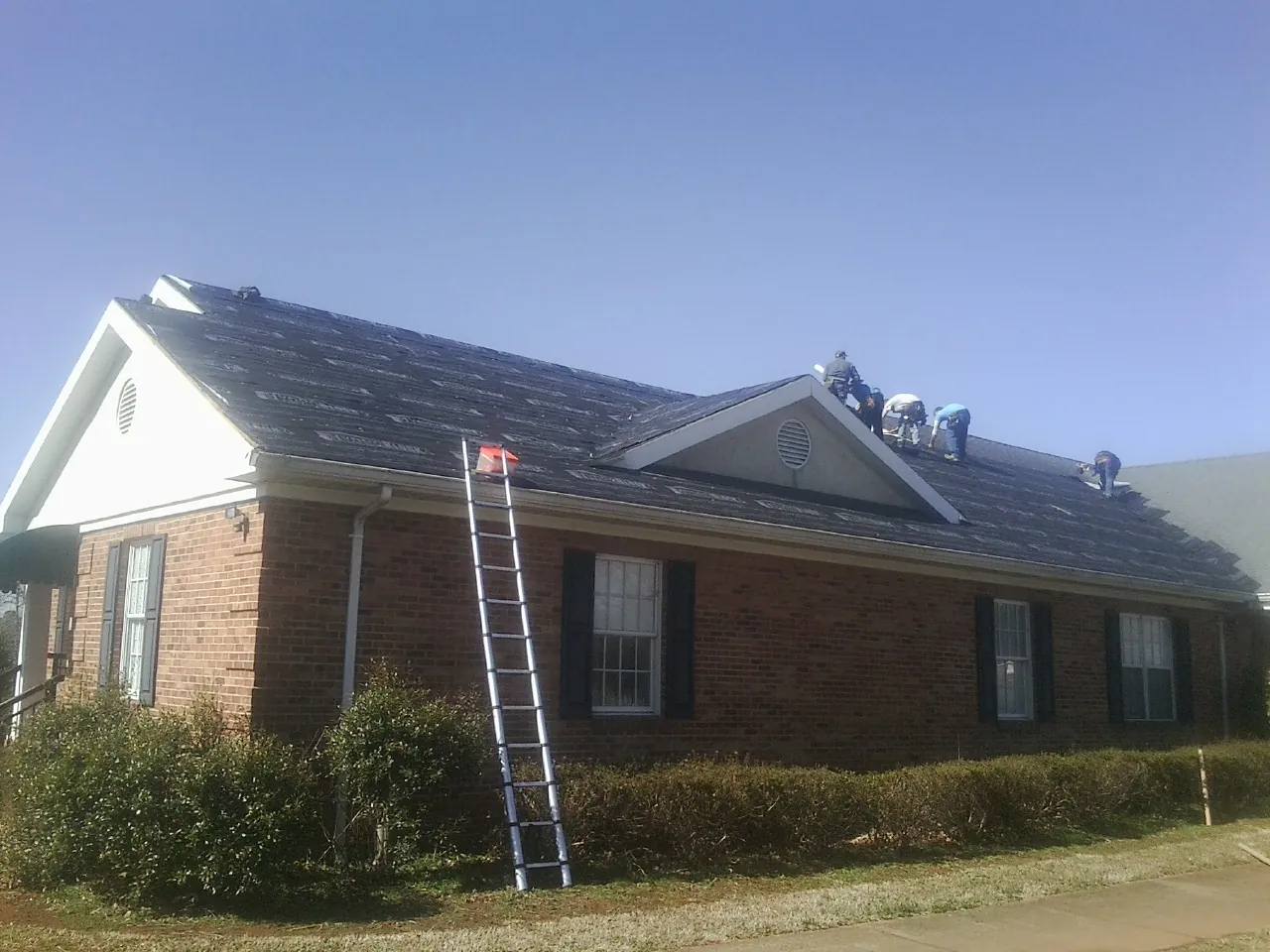 Crew tearing shingles off a brick ranch roof with a ladder set — Metal Roof Repair work by our crew in Crocheron