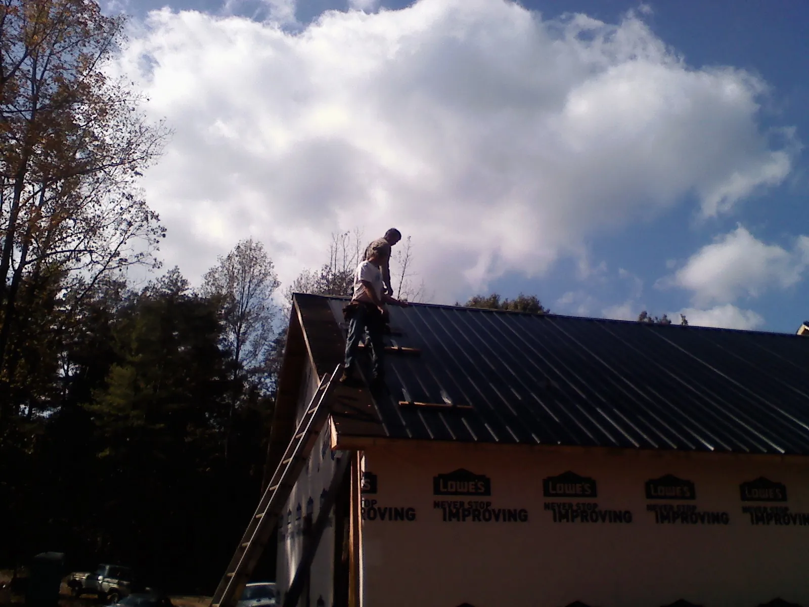 Roofer fastening dark metal panels high against a cloudy sky, from a Roof Inspection job in Crocheron